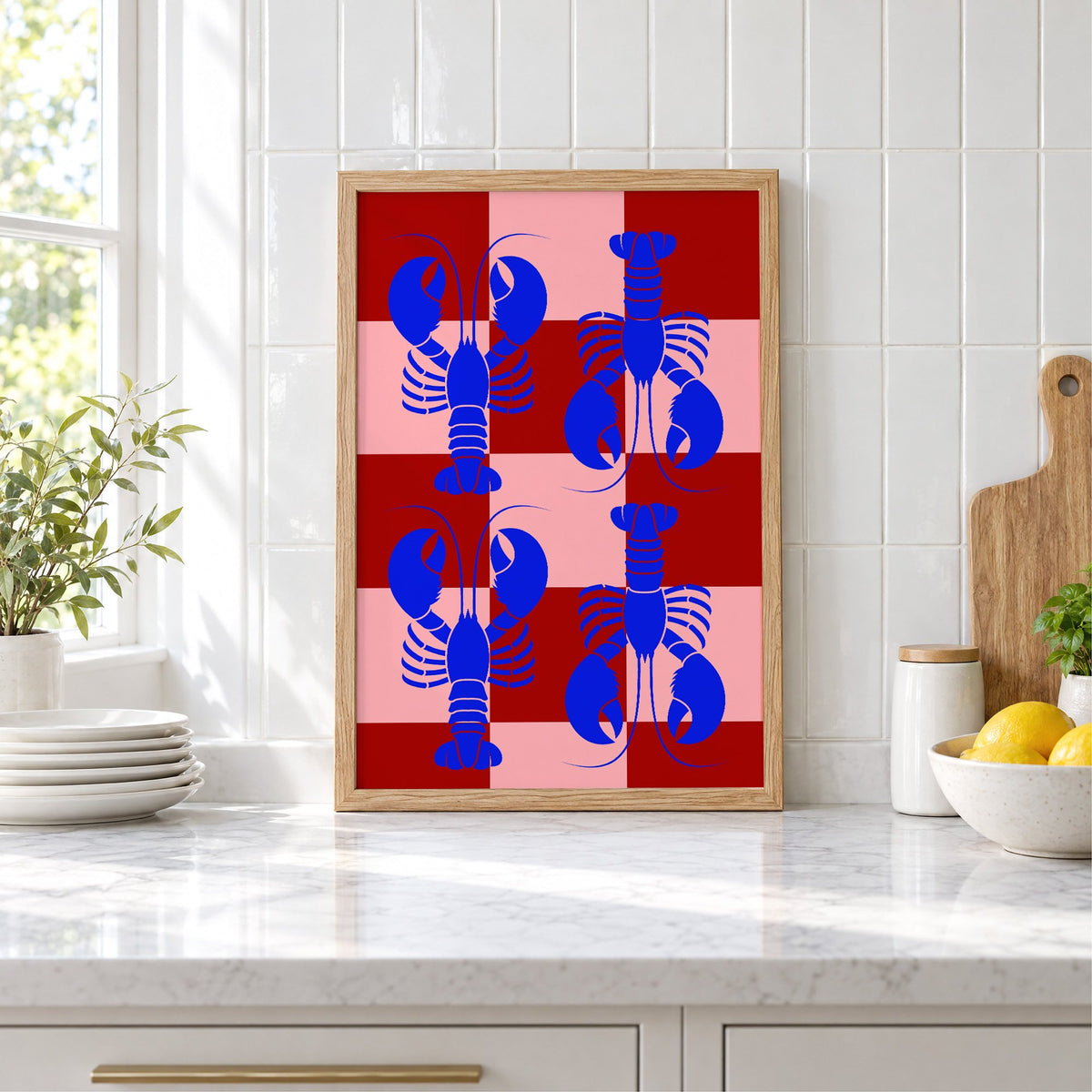 Blue lobster red pink checker print in an oak frame leaning on a marble counter by white tiles and lemons