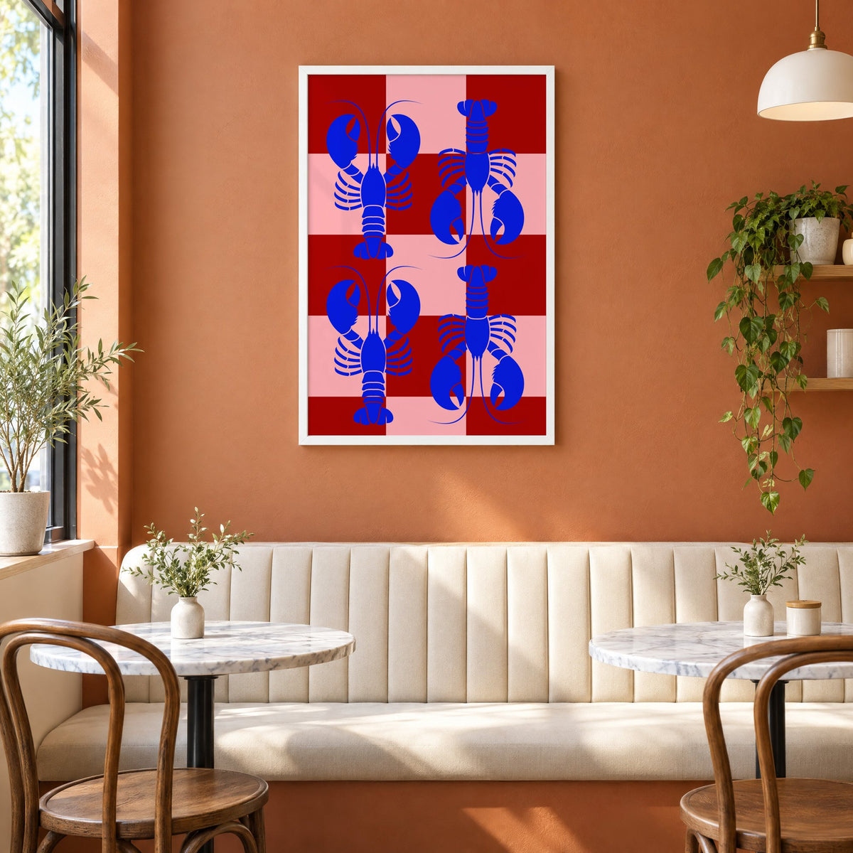 Blue lobster red pink checker print in a white frame above a cream banquette on a terracotta cafe wall