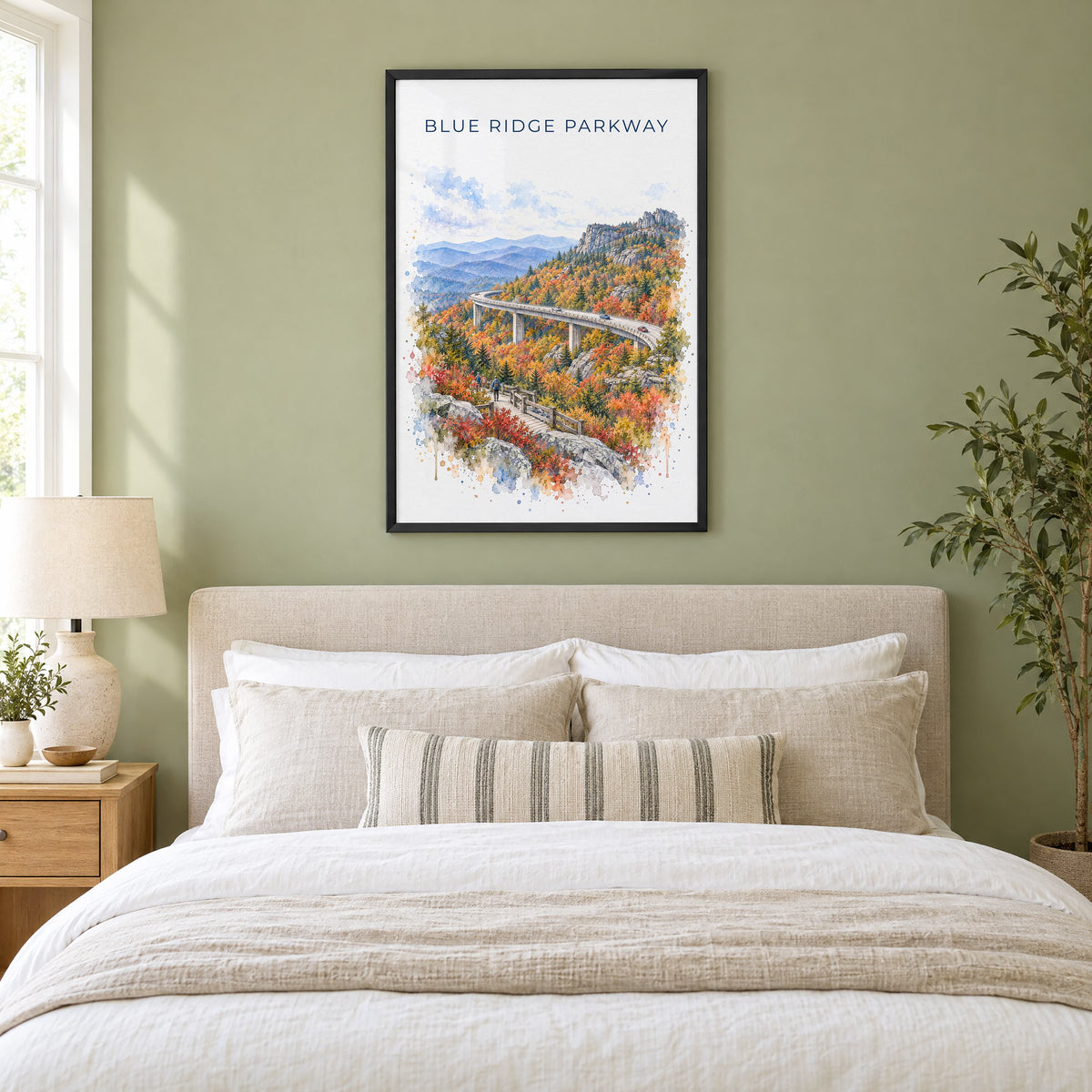 Blue Ridge Parkway watercolor print in a black frame above an upholstered headboard in a sage green bedroom