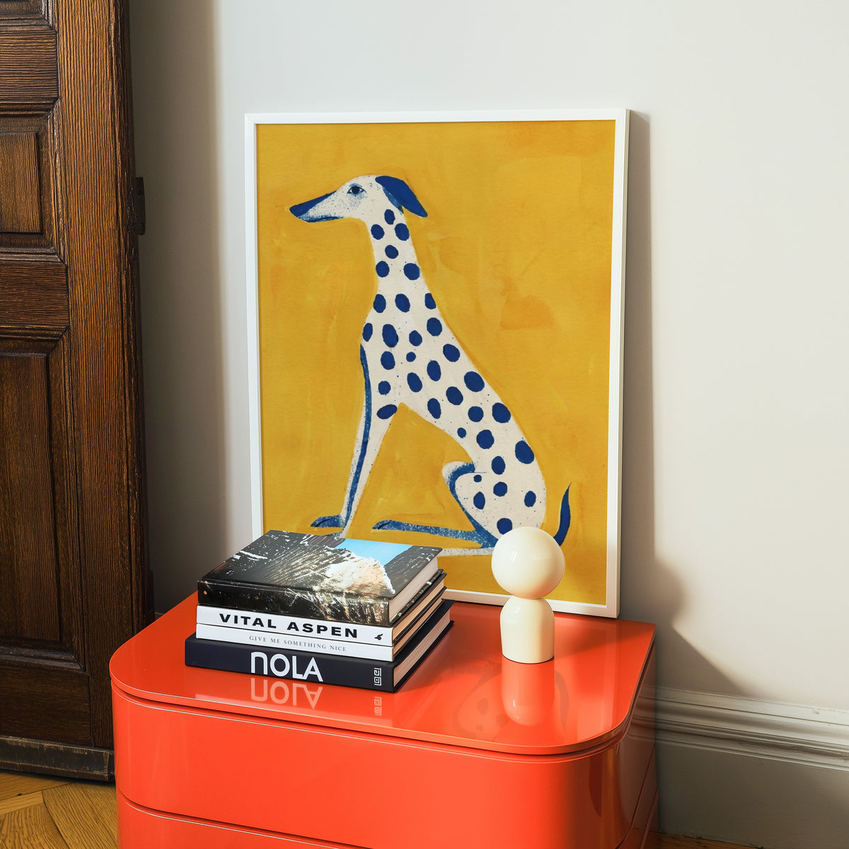 Cobalt spotted hound print in a white frame on a glossy orange cabinet with books