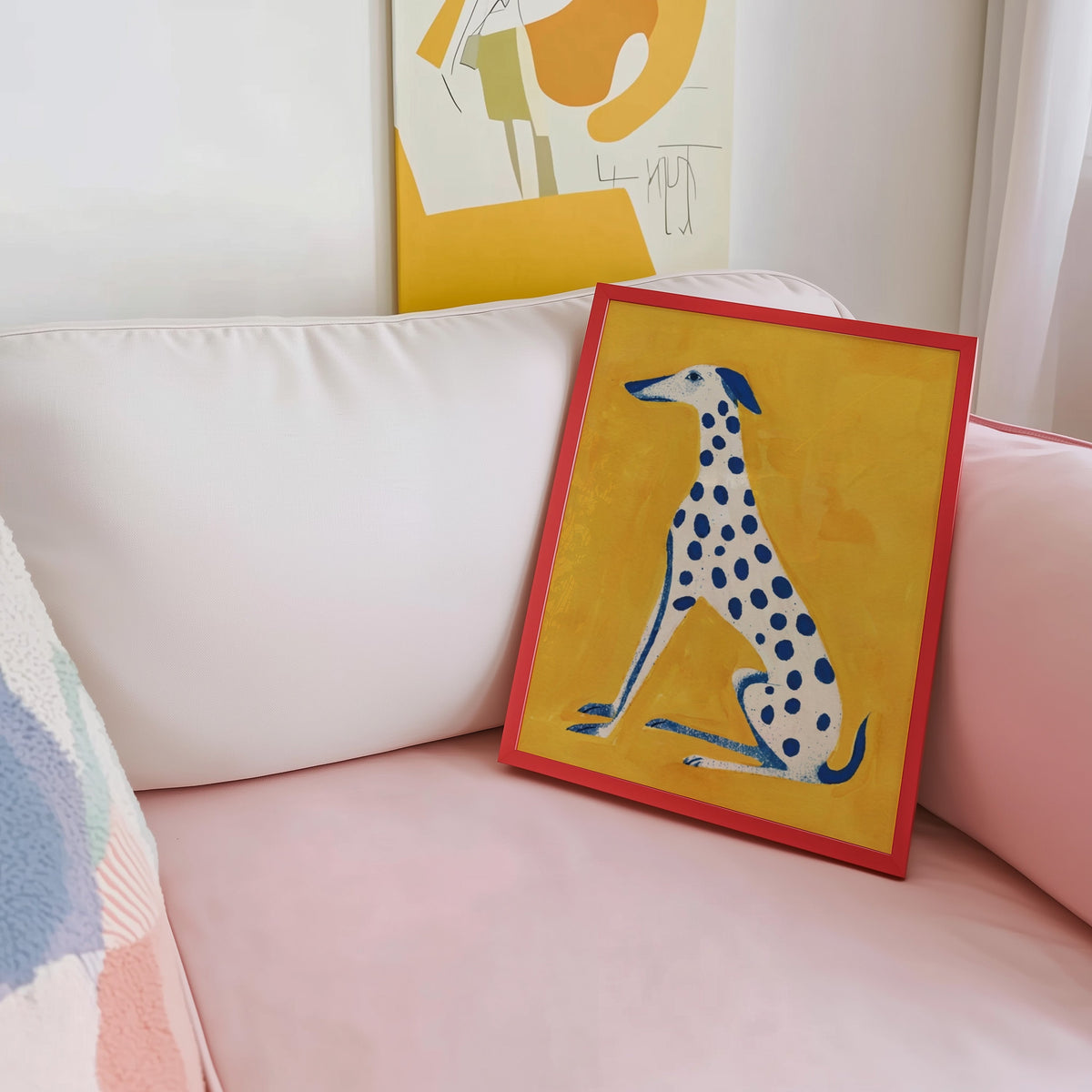 Blue and yellow dog print shown in a red frame leaning on a blush pink sofa