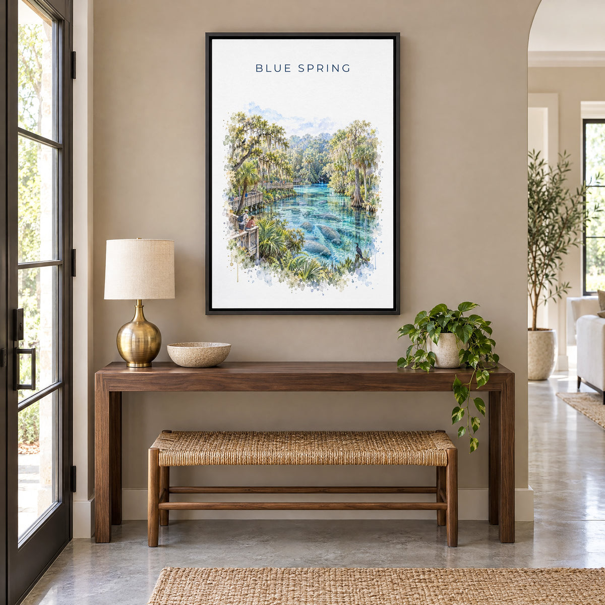 Blue Spring State Park watercolor print as a black floater canvas above a walnut console and woven bench in an entryway