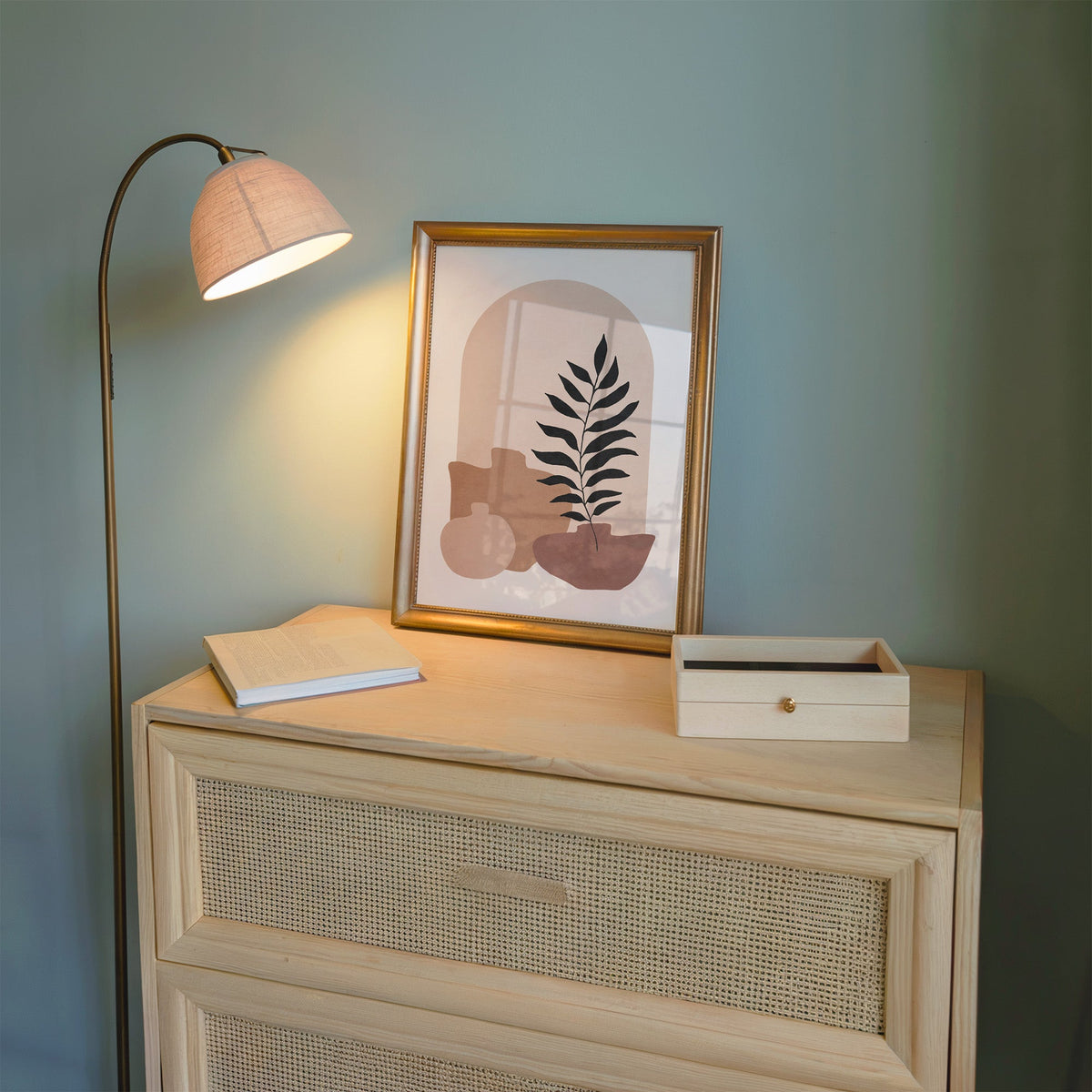 Blush arch and three vases boho botanical print shown in a gold frame on a cane dresser lit by a floor lamp