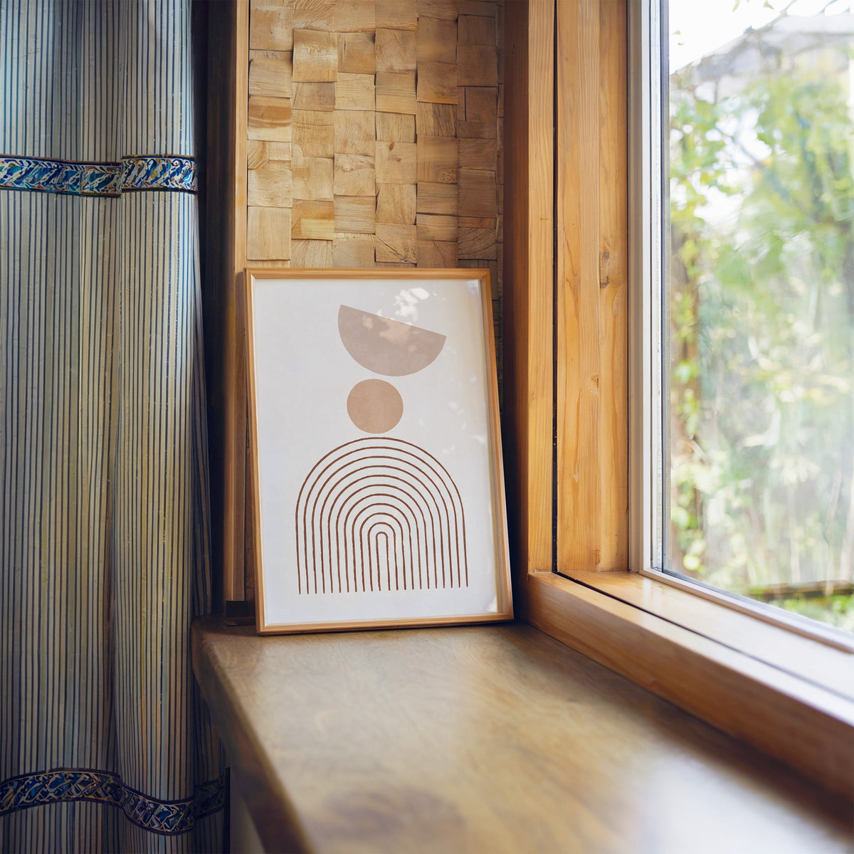 Blush half moon and rust line arch boho print in a light wood frame leaning on a wooden window sill by a garden view