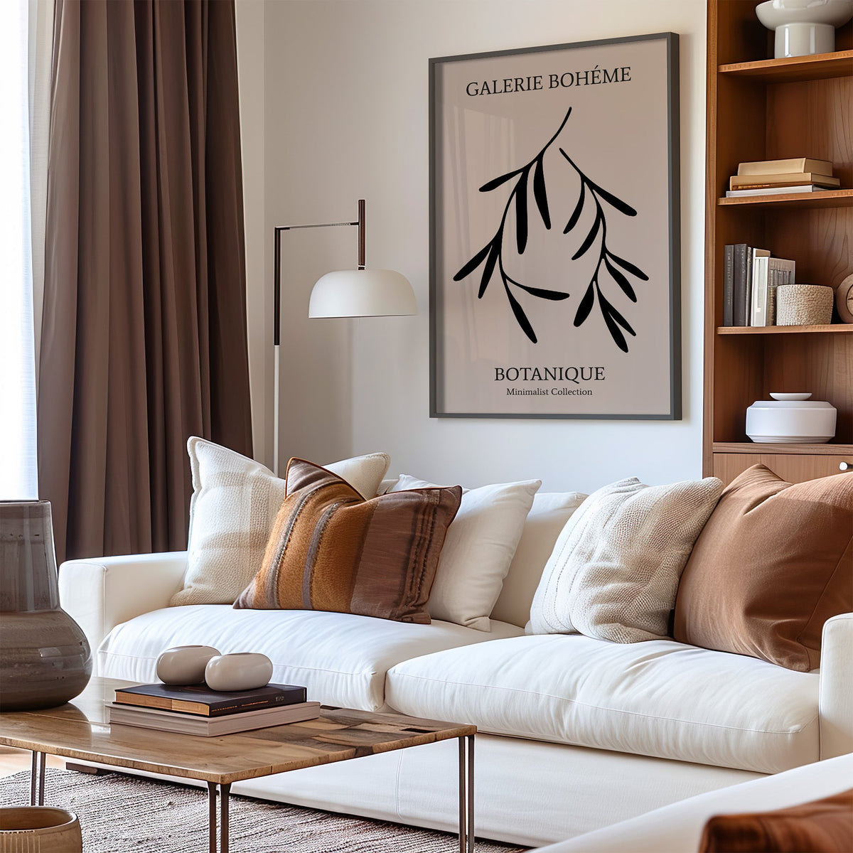 Two black hanging branches on blush botanical print in a black frame above a cream sofa with brown striped pillows