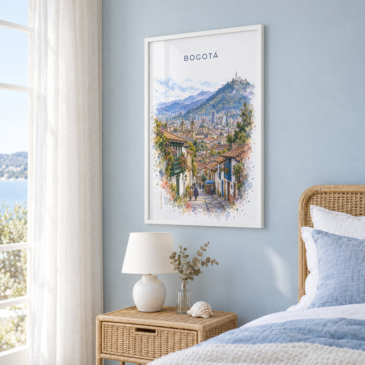 Bogotá watercolor print in a white frame on a pale blue wall beside a rattan bed in a coastal bedroom