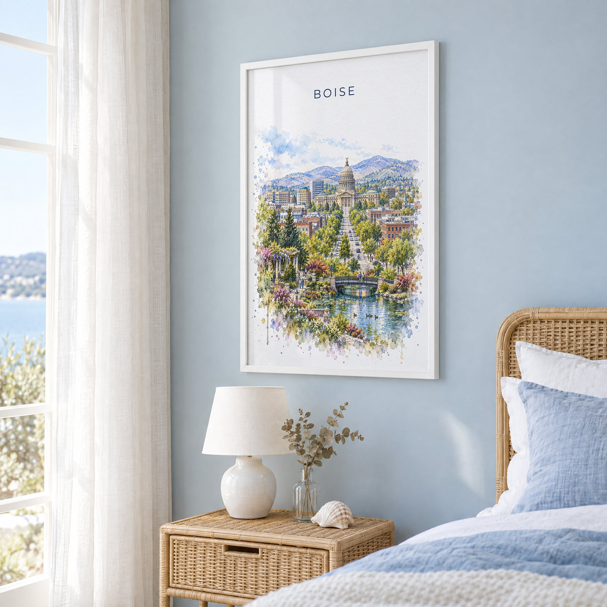 Boise watercolor print in a white frame on a pale blue wall beside a rattan bed in a coastal bedroom