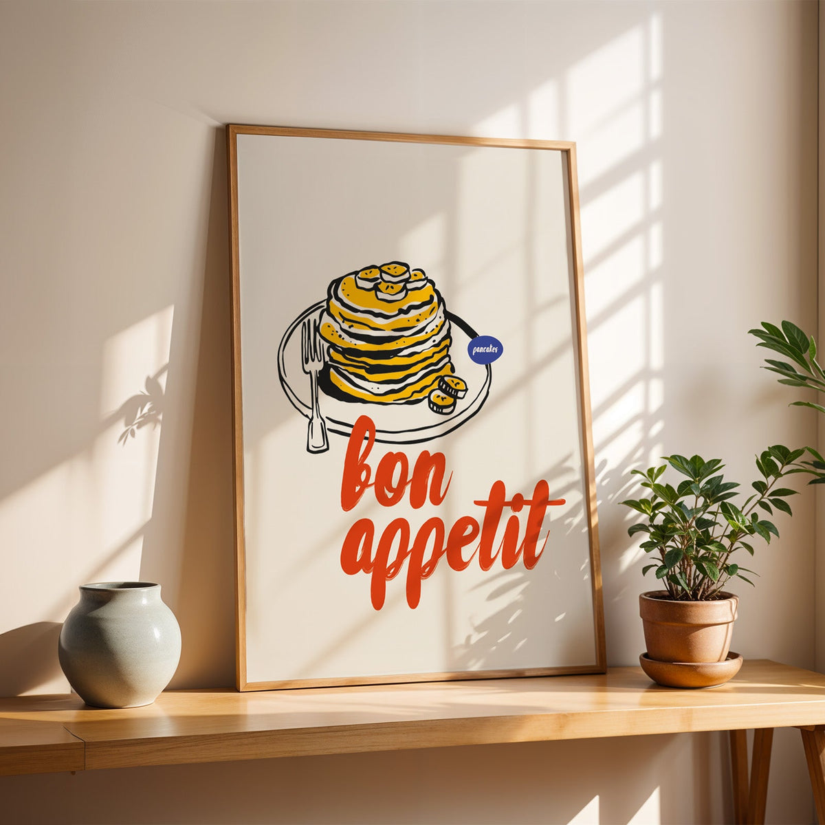 Bon Appetit pancakes print in a slim oak frame on a console with a grey-blue vase