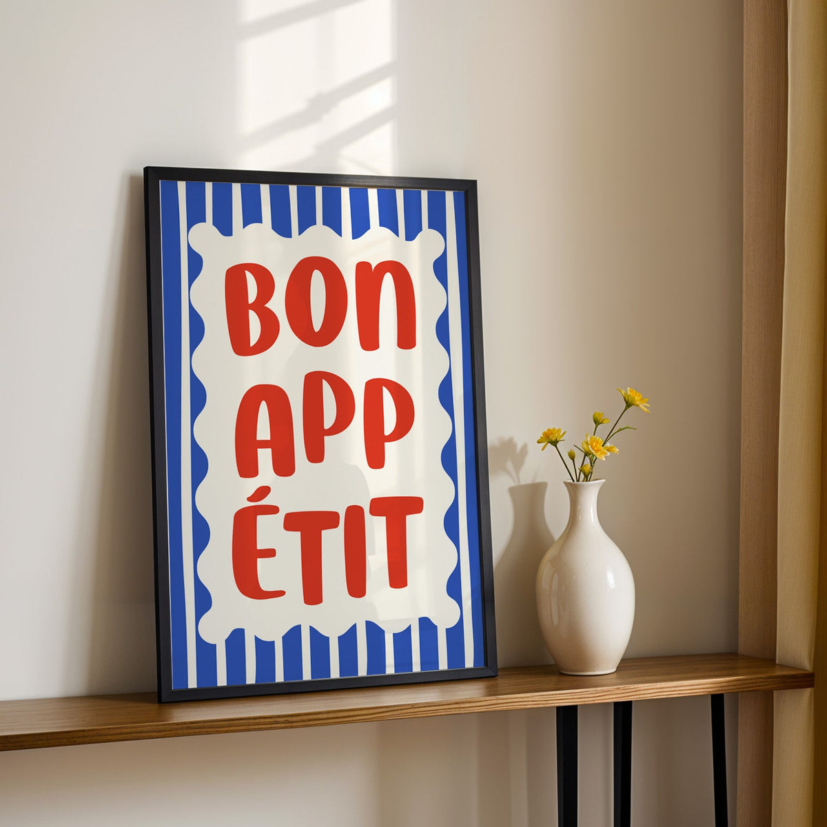 Bon appetit print in a black frame on a console table with yellow daisies