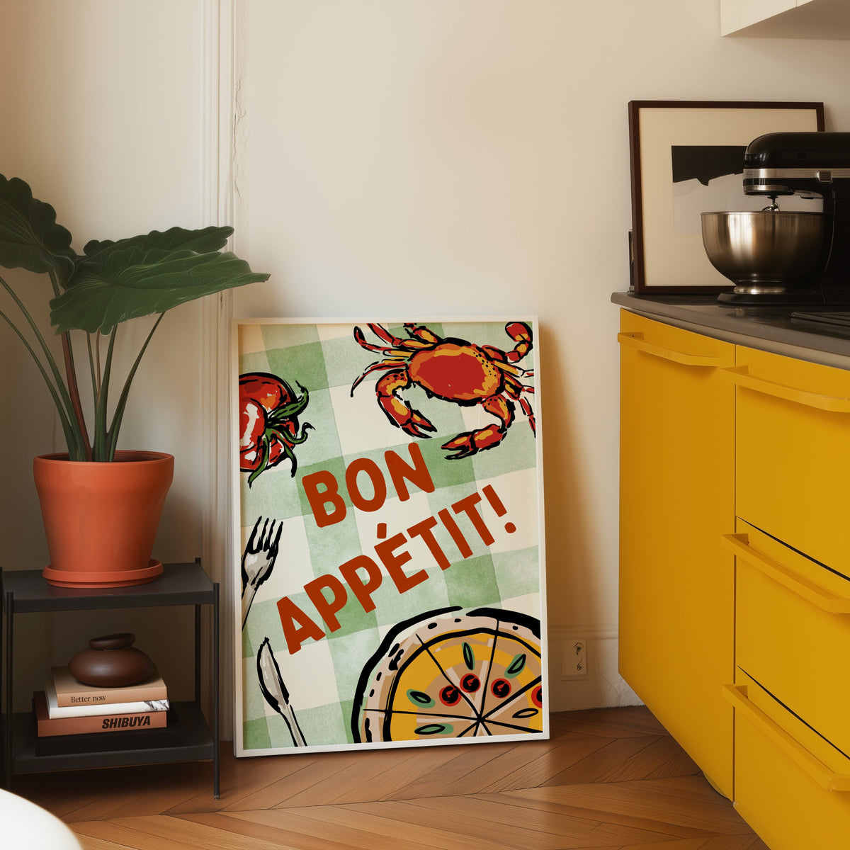Bon Appetit crab print in a white frame leaning on parquet beside a bright yellow kitchen