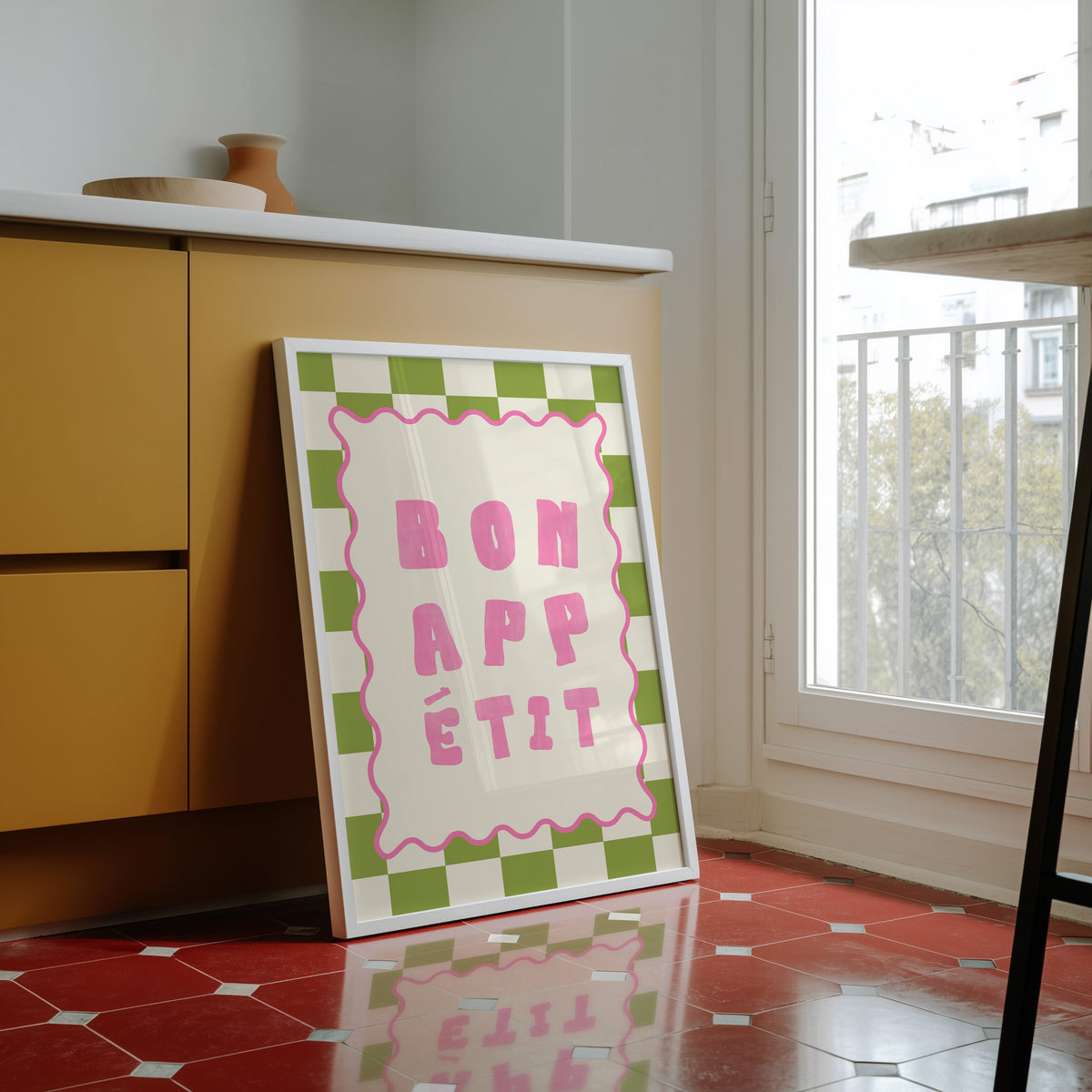 Bon Appetit check print in a white frame against yellow cabinets on a red tiled floor