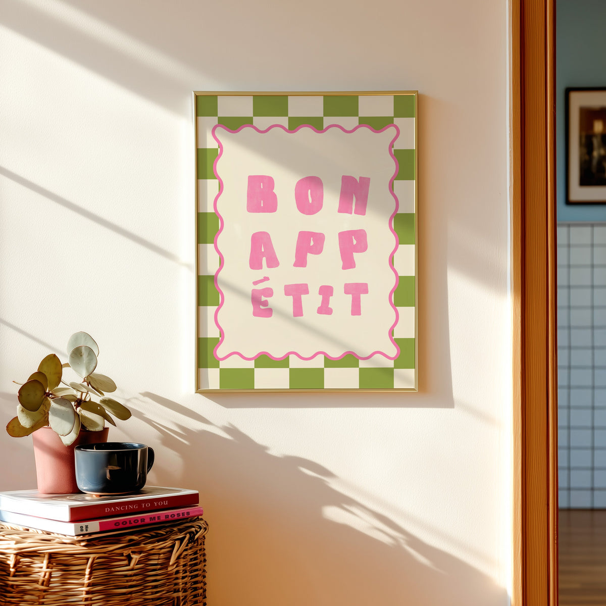 Bon Appetit check print shown in a gold frame above a basket of books and a pilea plant