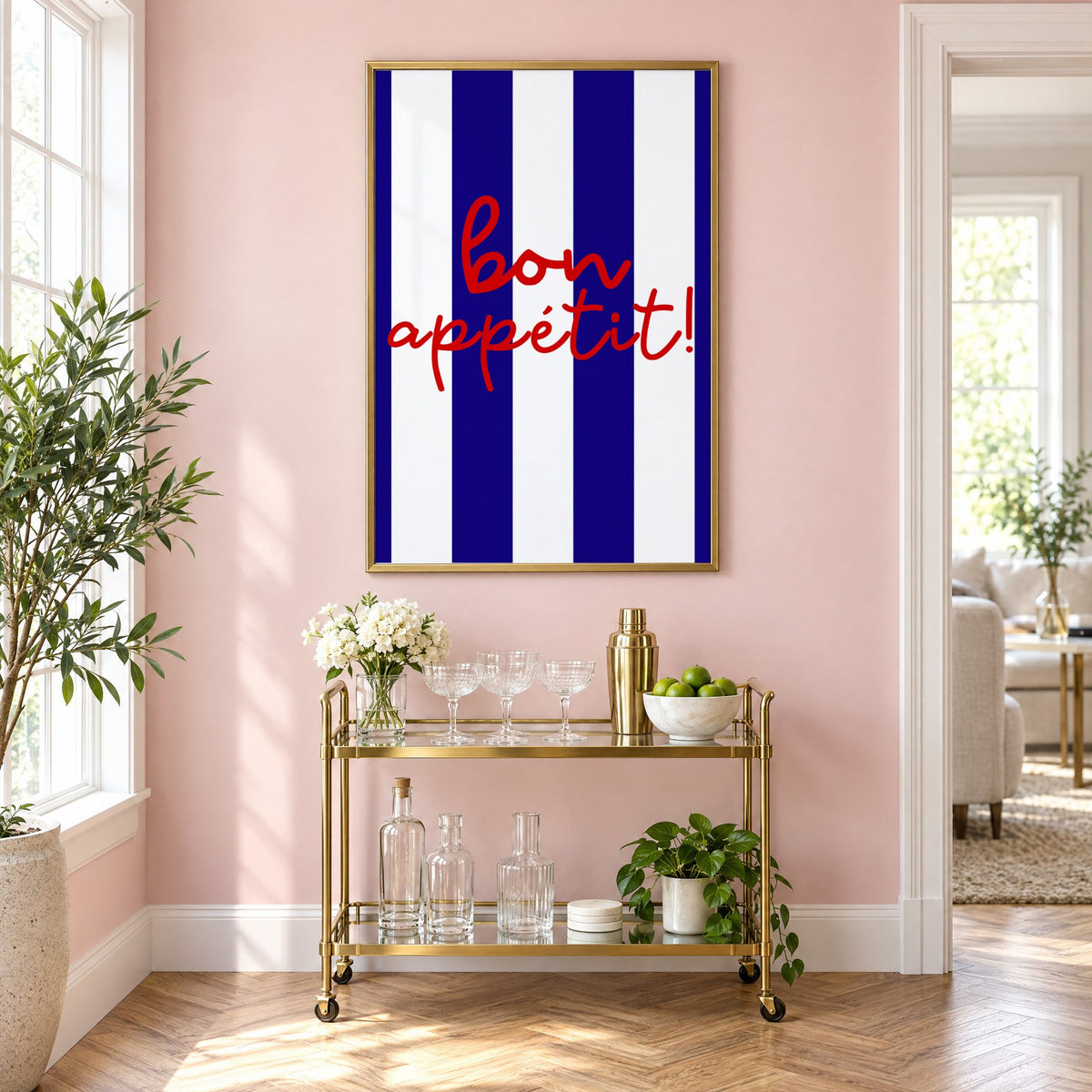 Bon appétit navy stripe print in a brass frame above a gold bar cart on a blush pink wall