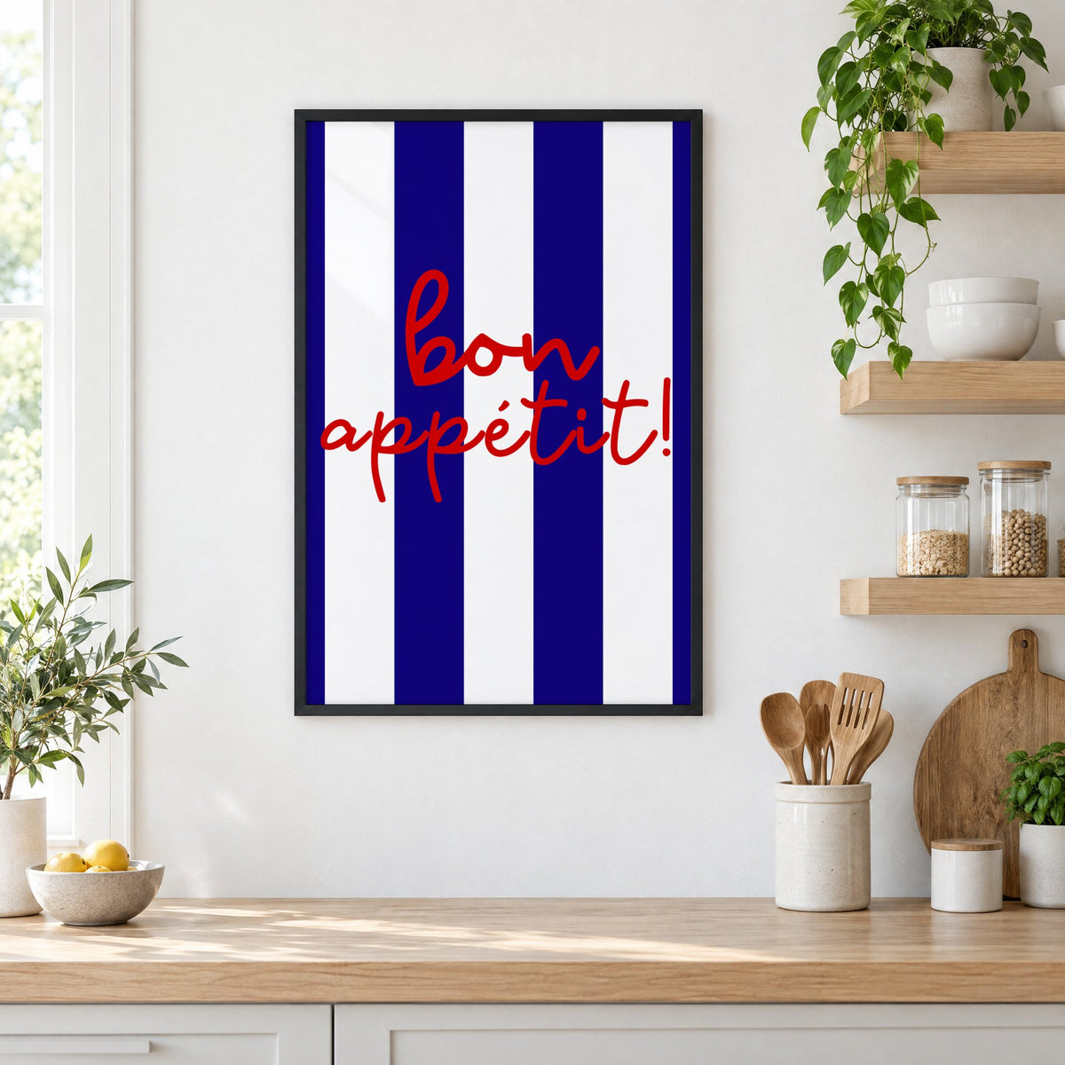 Bon appétit navy stripe print in a black frame in a white kitchen beside open wood shelves and glass jars