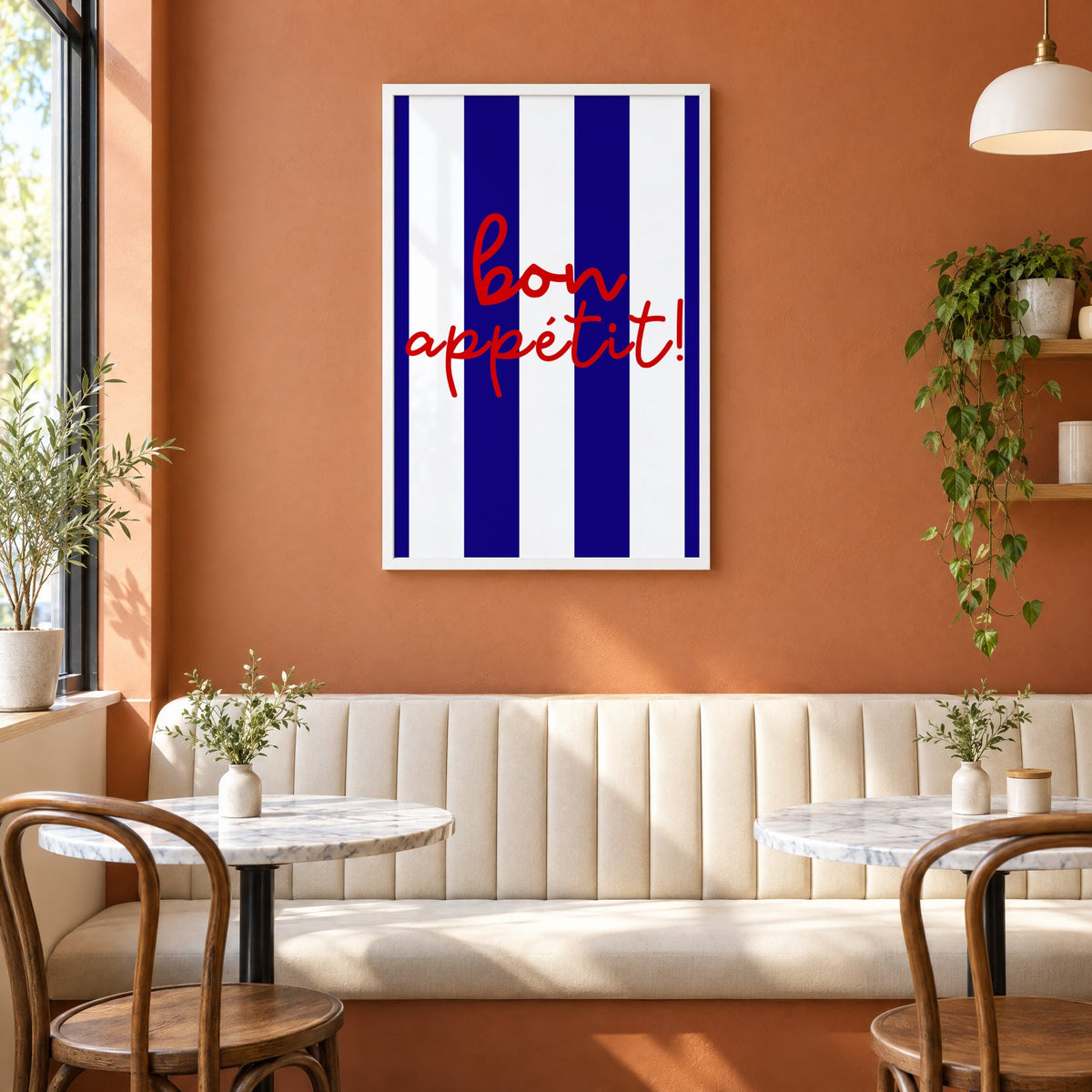 Bon appétit navy stripe print in a white frame above a cream banquette on a terracotta cafe wall