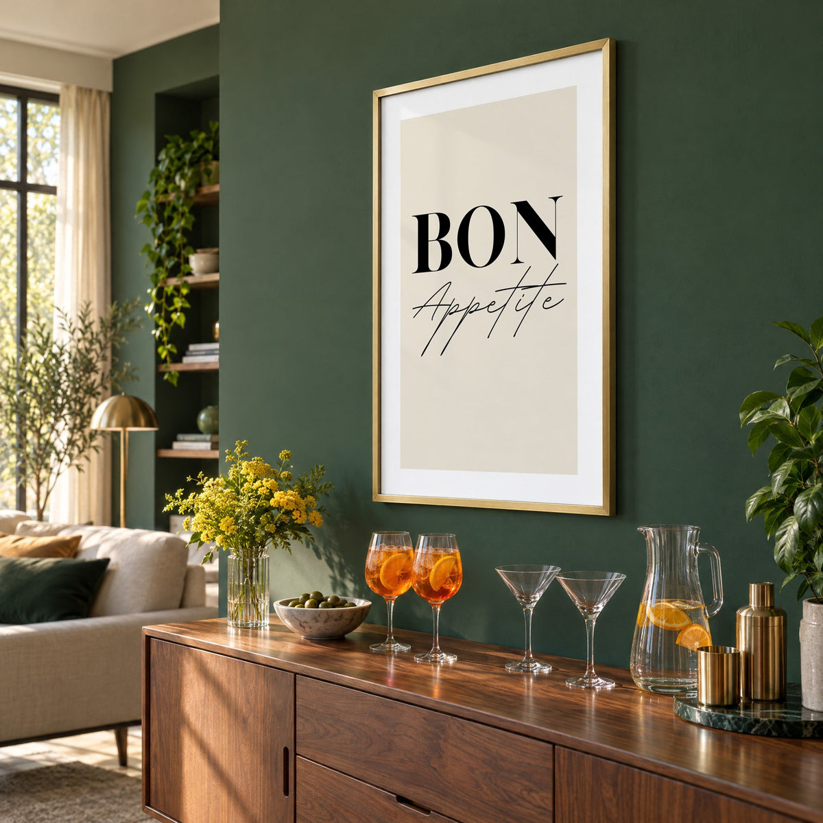 BON Appetite serif and script print in a brass frame on a bottle green wall above a sideboard with spritz and martini glasses, seen at an angle