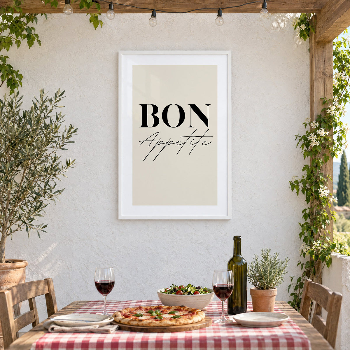 BON Appetite serif and script print in a white frame on a stucco wall above a checked-cloth table with pizza and red wine