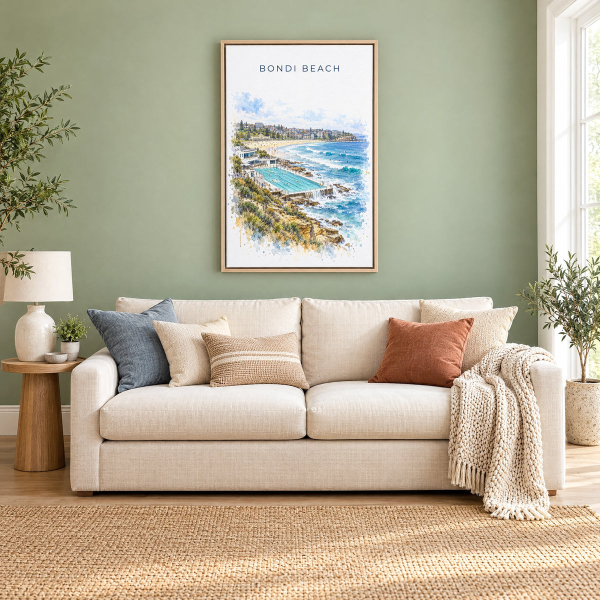 Bondi Beach watercolor print as a natural floater canvas above a cream linen sofa on a sage green wall