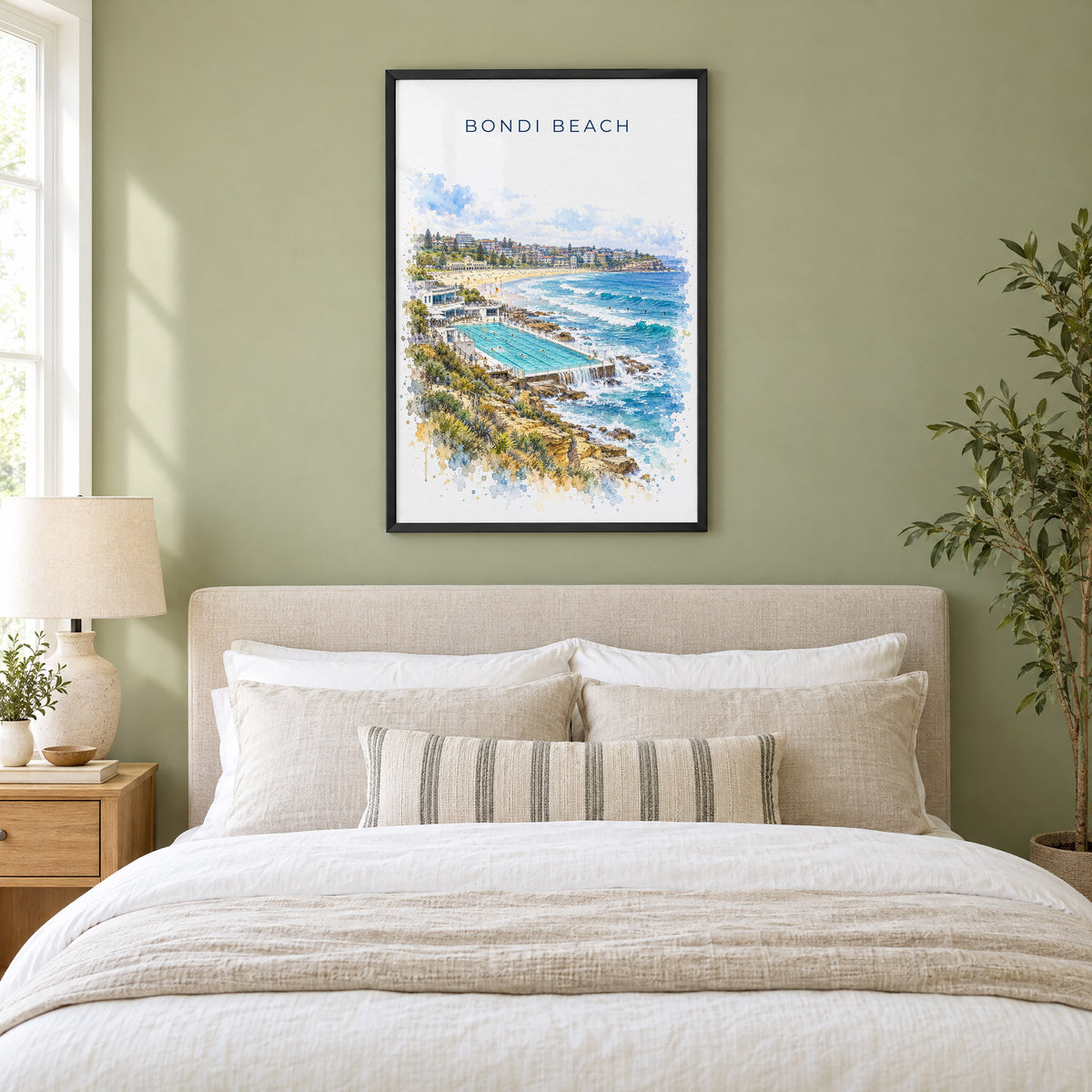 Bondi Beach watercolor print in a black frame above an upholstered headboard in a sage green bedroom