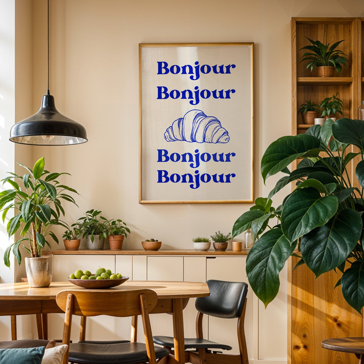 Bonjour croissant print in an oak frame in a dining room above a plant-lined sideboard