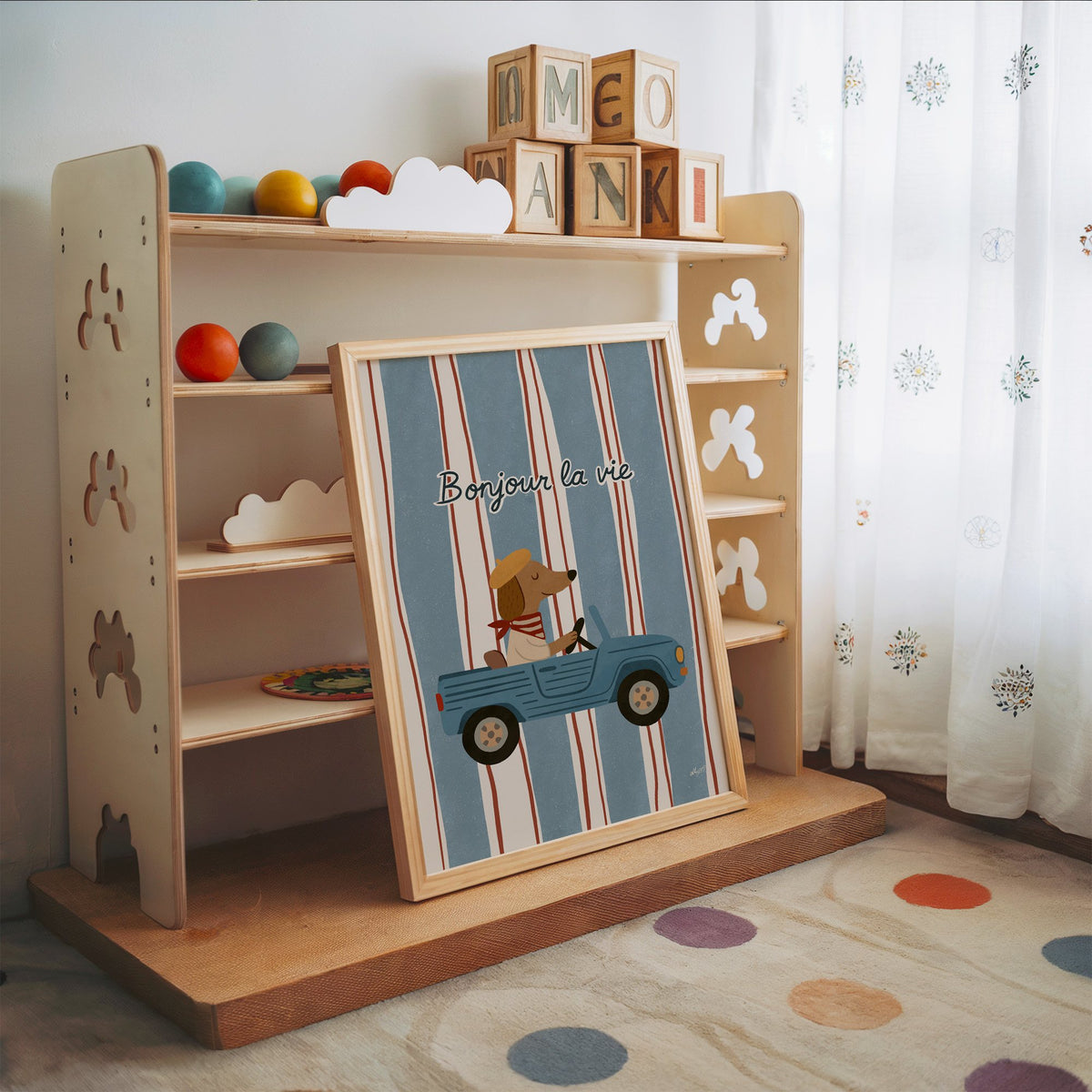Dog driving car with french script nursery print in an oak frame leaning on a toy shelf with wooden letter blocks