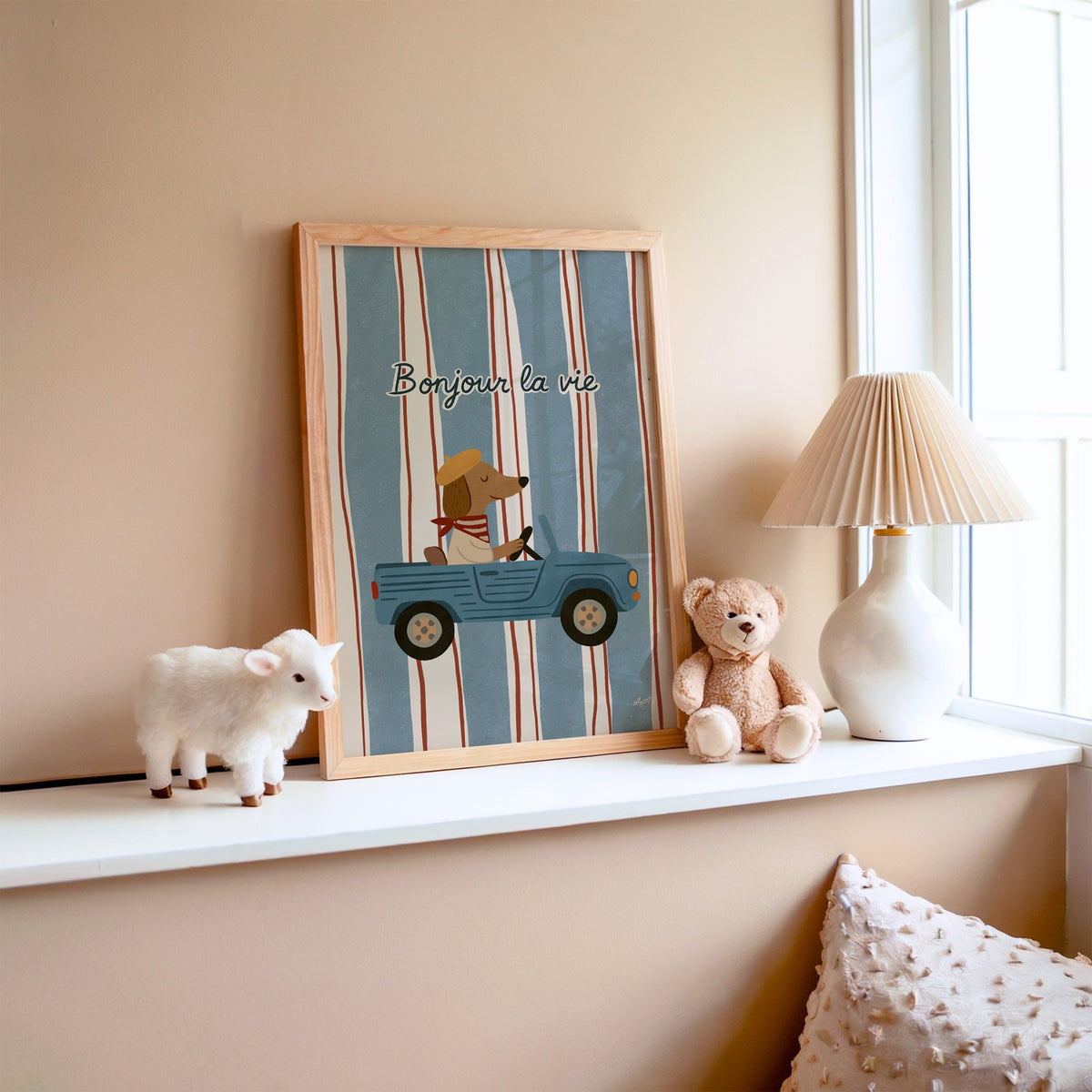 Dog driving car with french script nursery print in an oak frame on a window ledge with a toy lamb and teddy