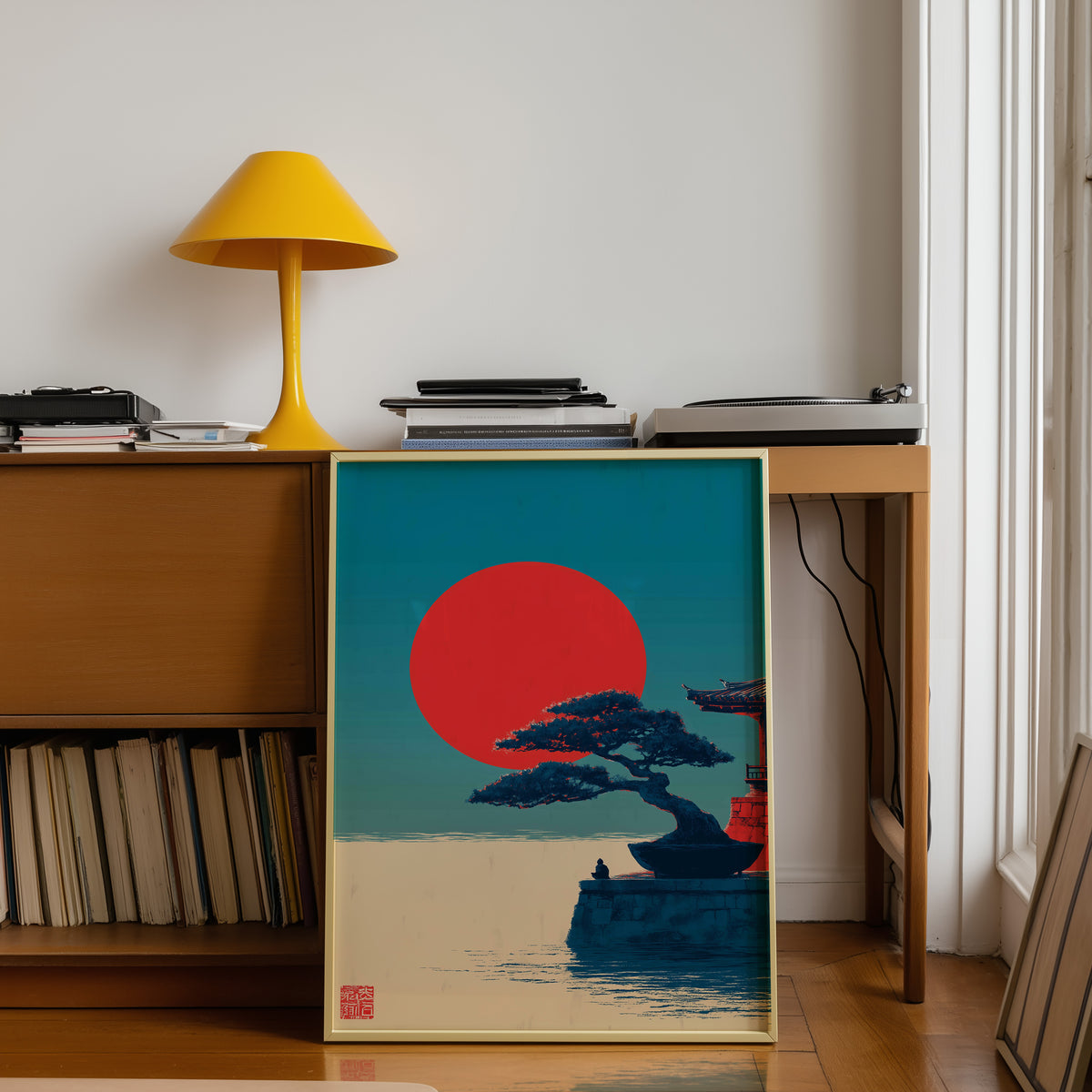 Bonsai pine under red sun print shown in a gold frame below a teak desk with a yellow lamp