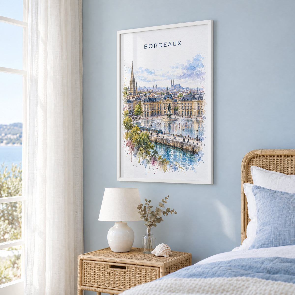 Bordeaux watercolor print in a white frame on a pale blue wall beside a rattan bed in a coastal bedroom