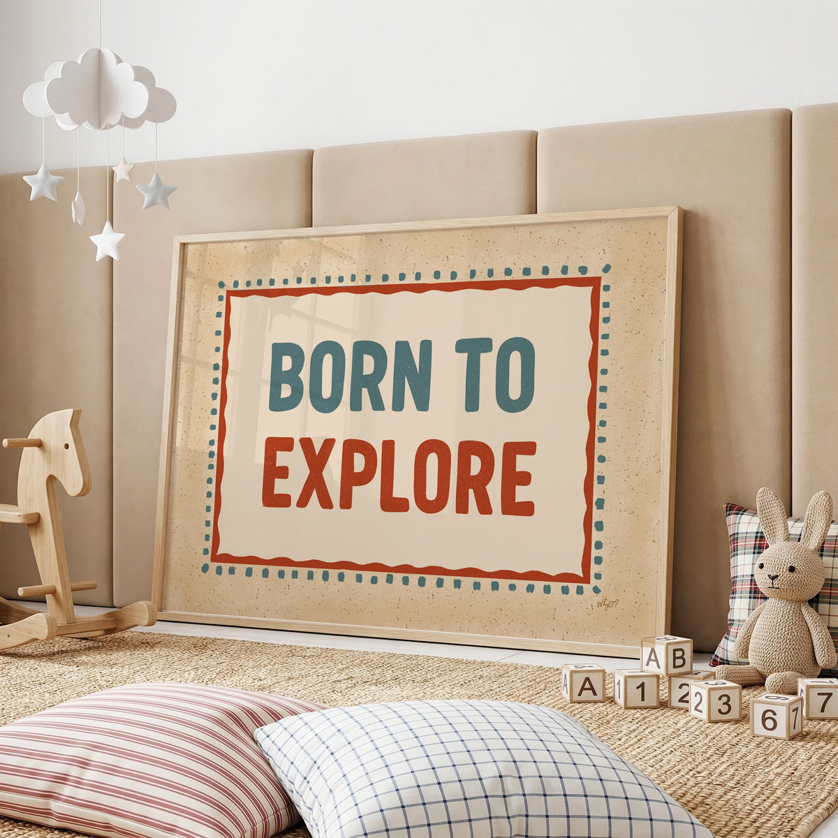 Born to explore retro quote nursery print in an oak frame on a padded wall by a wooden rocking horse