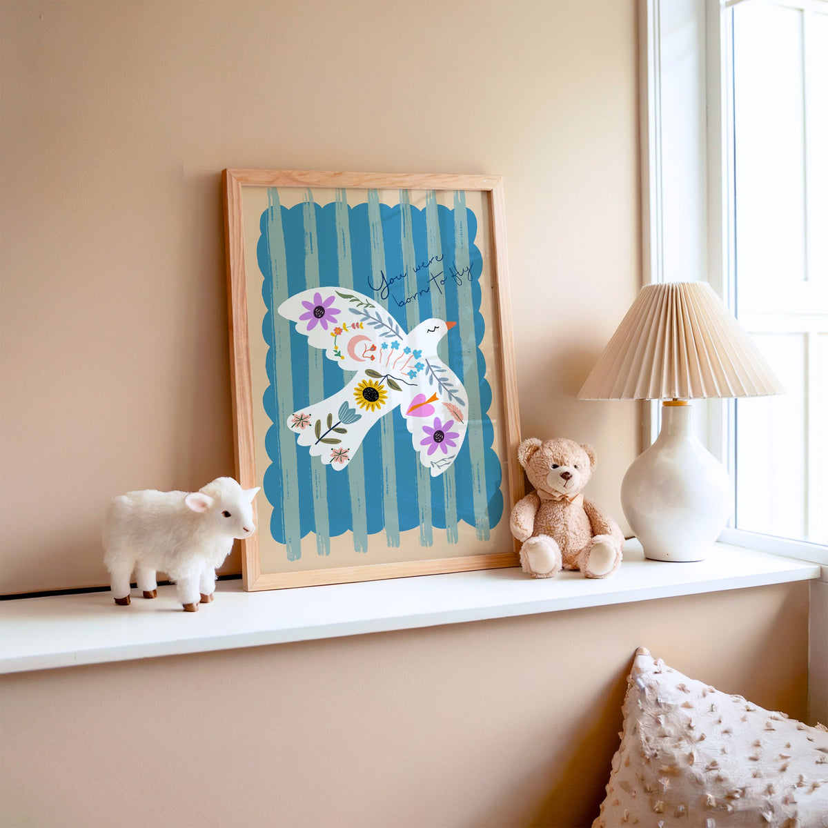 White dove covered in flowers nursery print in an oak frame on a window ledge with a toy lamb and teddy
