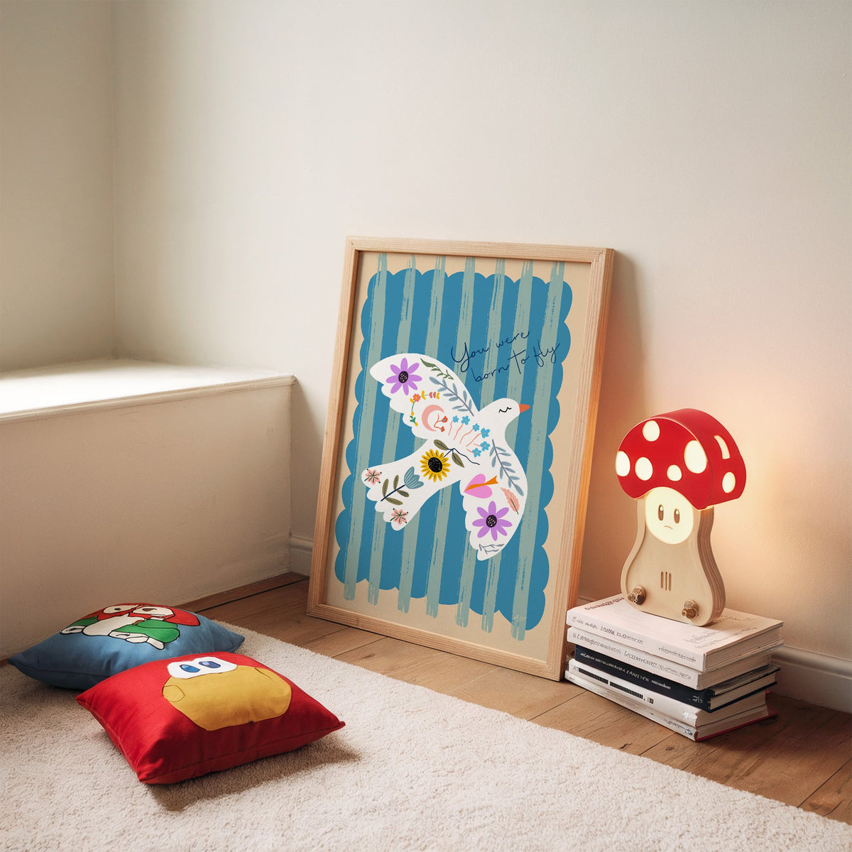 White dove covered in flowers nursery print in an oak frame leaning on a rug beside a mushroom lamp and floor cushions