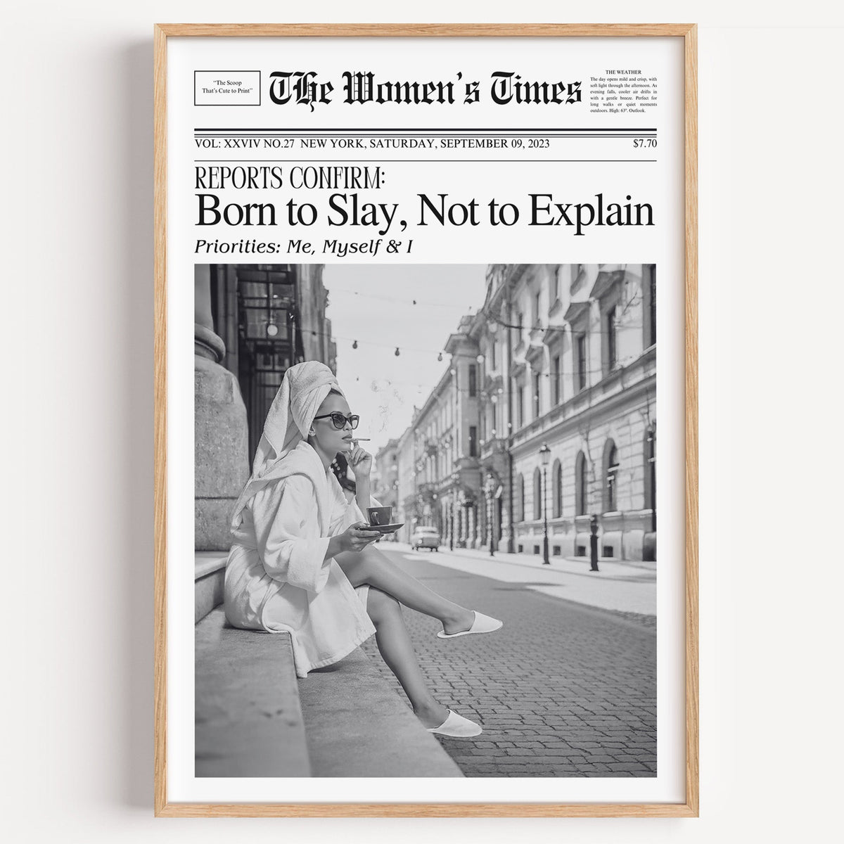 Mock front page with woman in robe on a cobbled street print in a light oak frame on a plain white wall