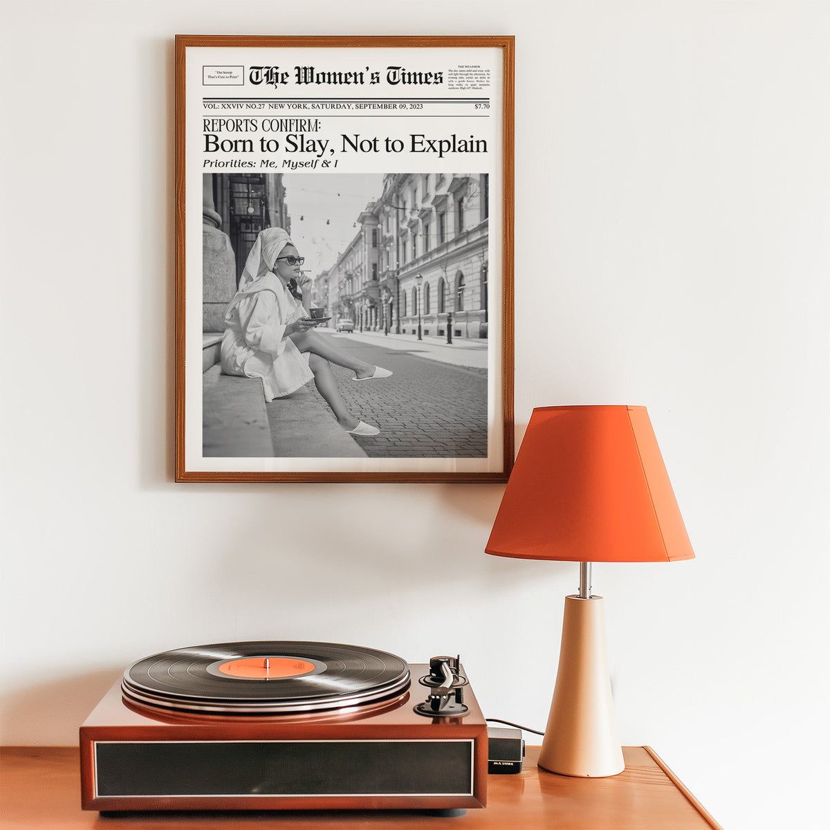 Mock front page with woman in robe on a cobbled street print in a walnut frame above a record player and orange lamp