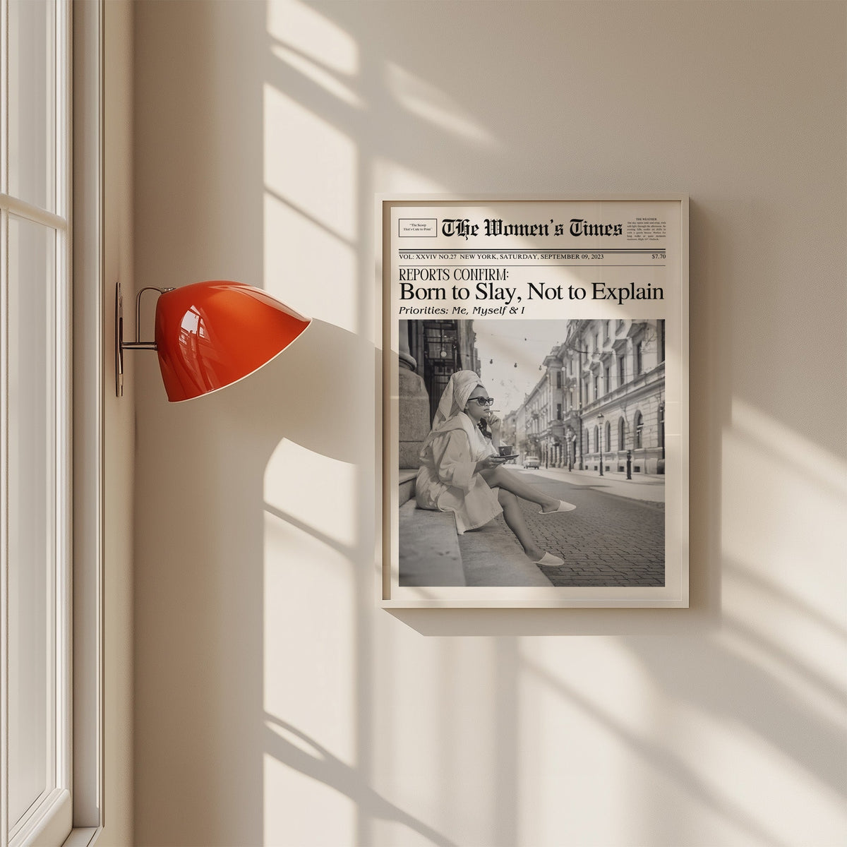 Mock front page with woman in robe on a cobbled street print in a white frame on a sunlit wall beside a red sconce