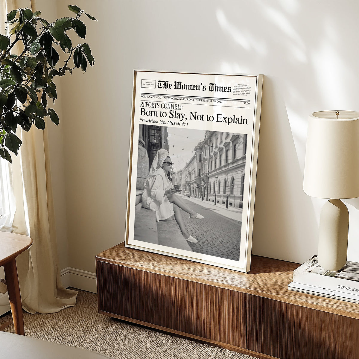 Mock front page with woman in robe on a cobbled street print in a white frame on a walnut sideboard beside a ceramic lamp