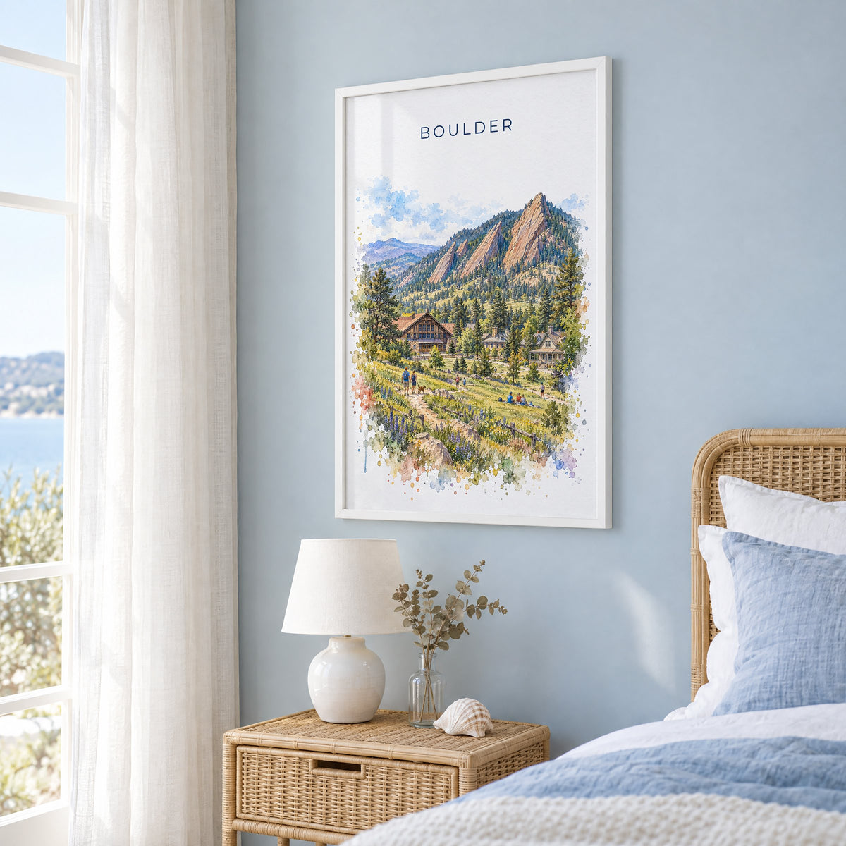 Boulder watercolor print in a white frame on a pale blue wall beside a rattan bed in a coastal bedroom