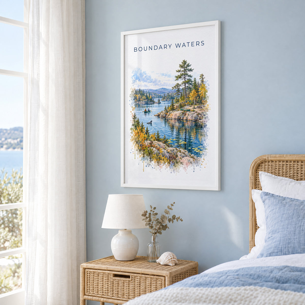 Boundary Waters watercolor print in a white frame on a pale blue wall beside a rattan bed in a coastal bedroom