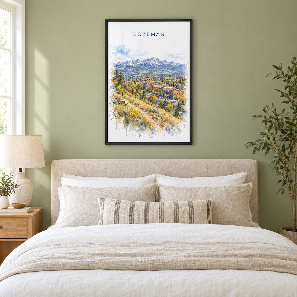 Bozeman watercolor print in a black frame above an upholstered headboard in a sage green bedroom