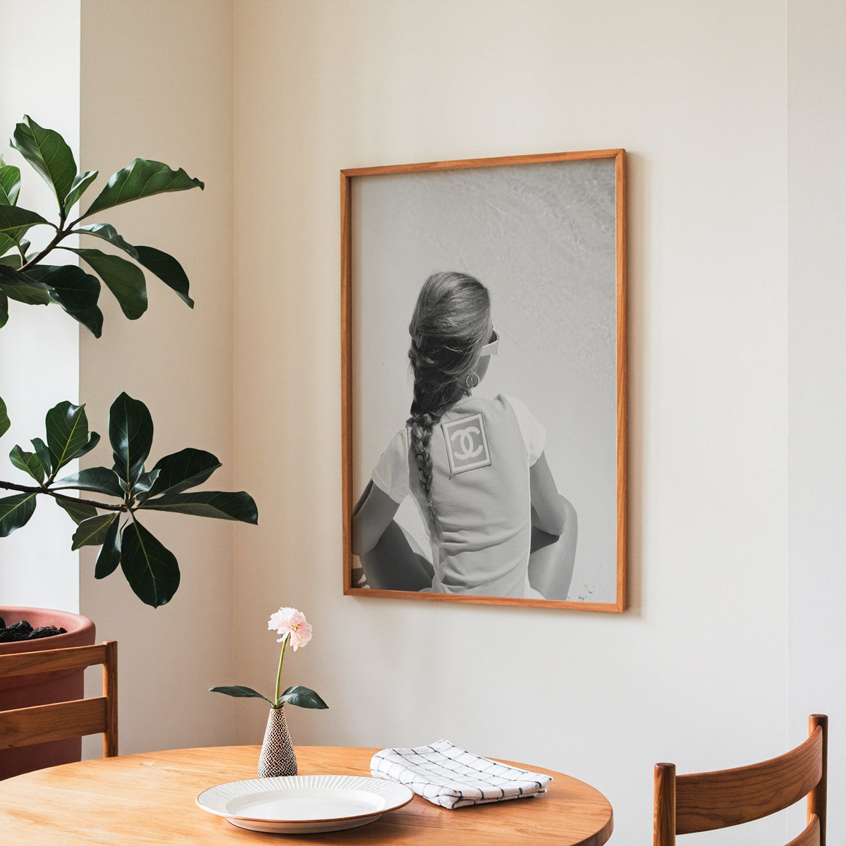 Woman with long braid seated on beach from behind print in a teak frame above a round wooden dining table