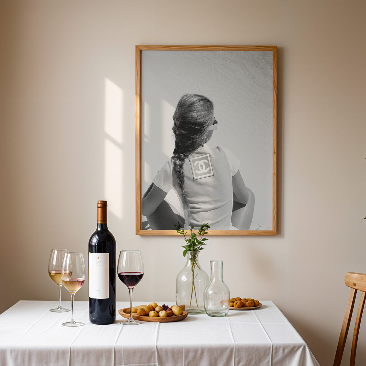 Woman with long braid seated on beach from behind print in an oak frame above a table set with red wine and glasses