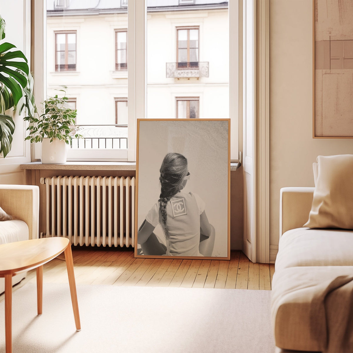 Woman with long braid seated on beach from behind print in an oak frame leaning by a French window in a living room