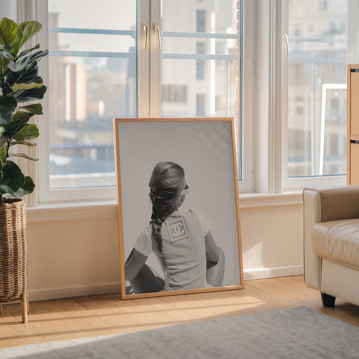 Woman with long braid seated on beach from behind print in an oak frame leaning on the floor beside a fiddle leaf fig