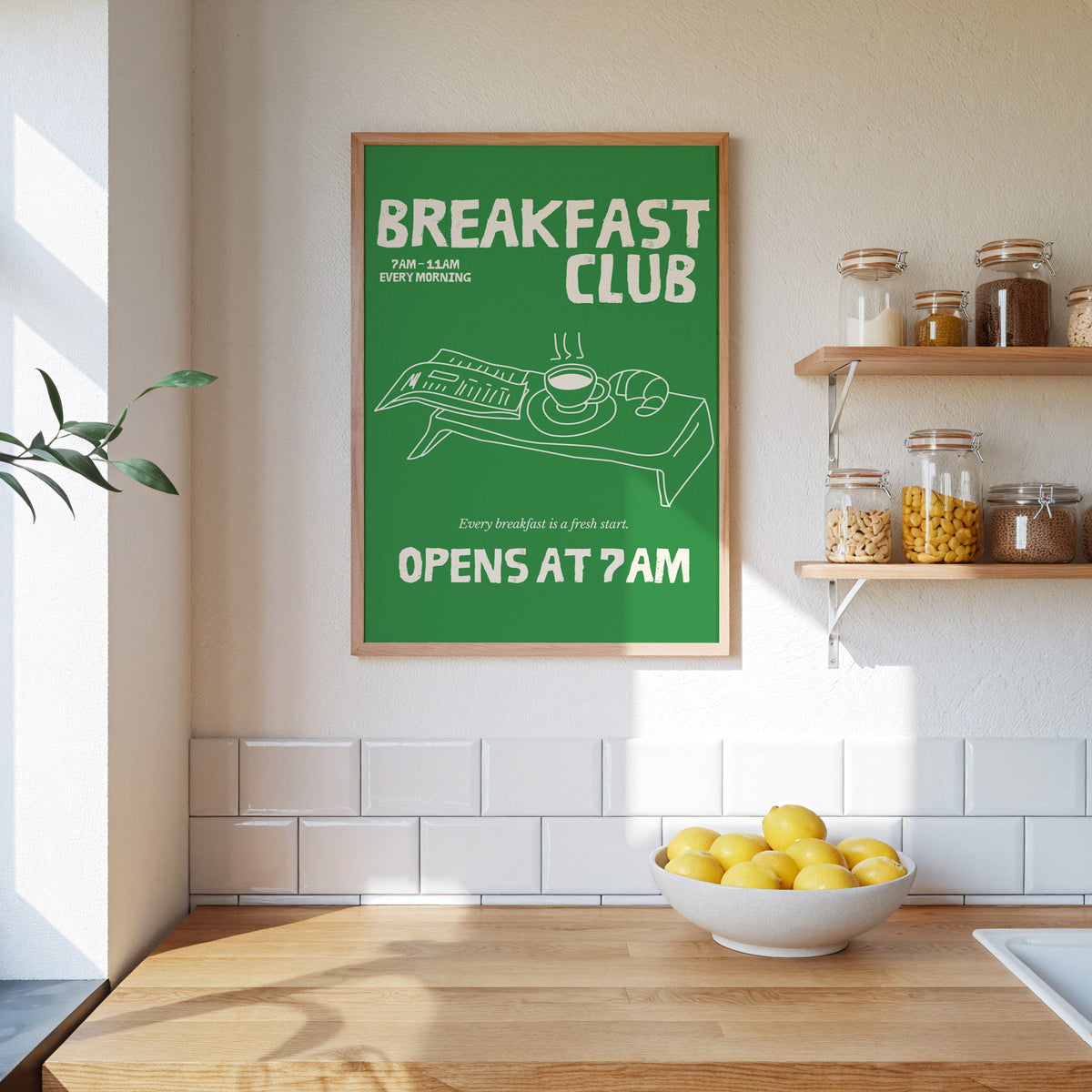 Breakfast Club green tray print in an oak frame on a subway-tiled kitchen wall beside open shelves of pantry jars