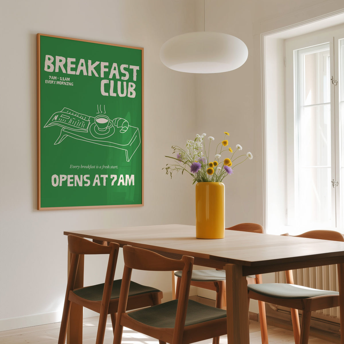 Breakfast Club green tray print in a slim oak frame above a wooden dining table under a round pendant light