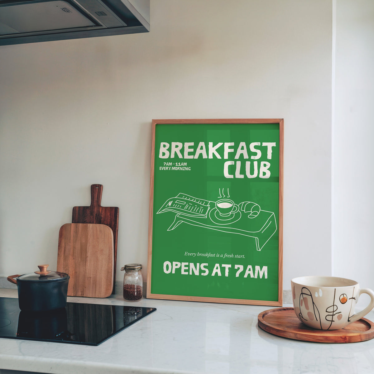 Breakfast Club green tray print in a pine frame leaning on a marble kitchen counter beside chopping boards