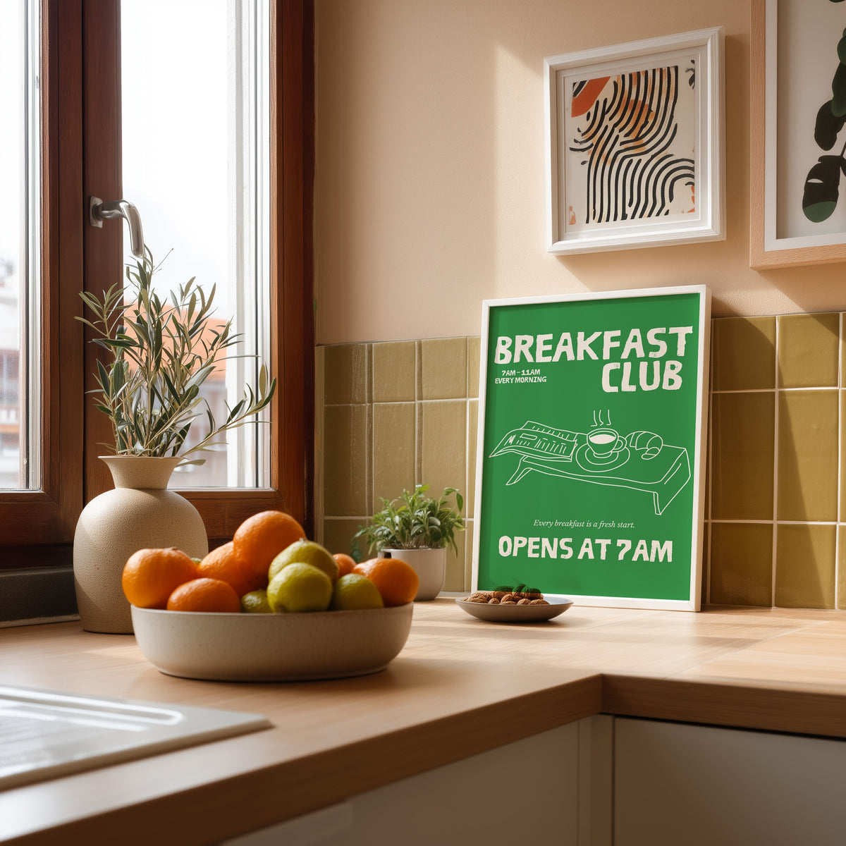 Breakfast Club green tray print in a white frame leaning against olive green kitchen tiles beside a bowl of citrus