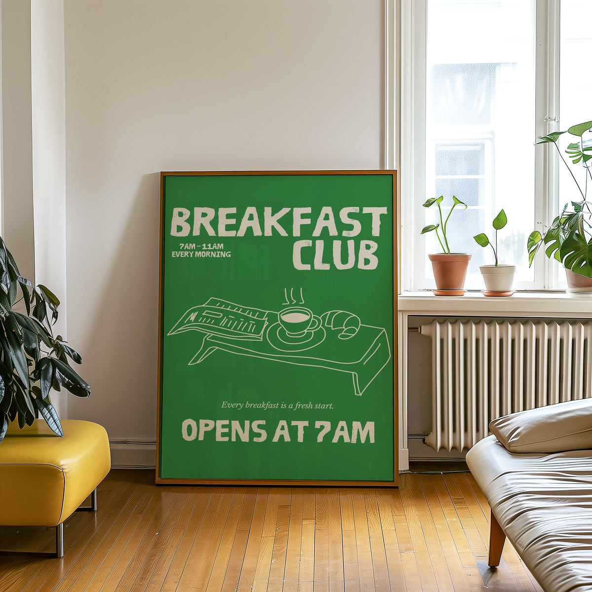 Breakfast Club green tray print in an oak frame leaning on a wooden floor beside a yellow leather bench
