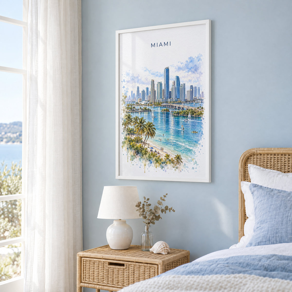 Brickell Miami watercolor print in a white frame on a pale blue wall beside a rattan bed in a coastal bedroom