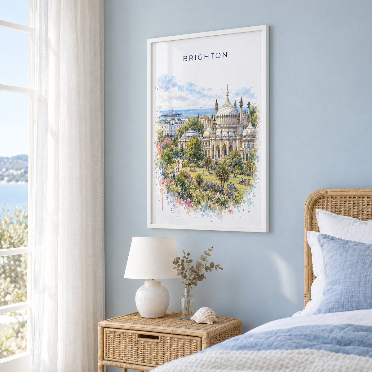 Brighton watercolor print in a white frame on a pale blue wall beside a rattan bed in a coastal bedroom