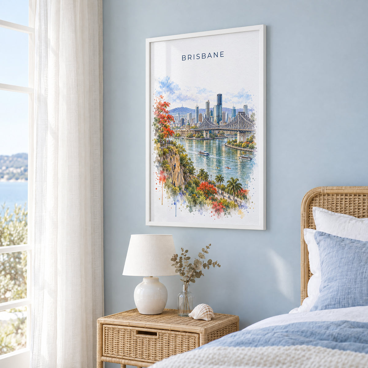 Brisbane watercolor print in a white frame on a pale blue wall beside a rattan bed in a coastal bedroom